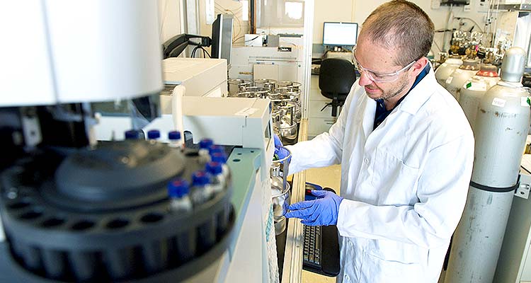 32880 Photo of a man in a white lab coat and safety glasses working in a laboratory.