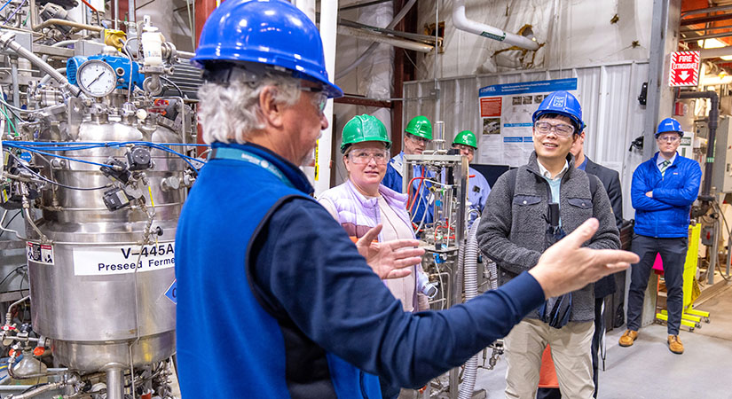 work-with-us-79360 Six people wearing hard hats and safety glasses on a tour in a lab.