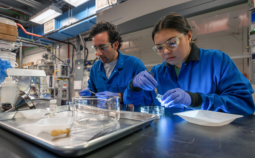 Two people wearing goggles working in a lab.