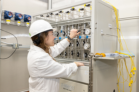 20250520-nrel-crysalis-biosciences-collaborate-to-scale-up-domestic-biomanufacturing-technologies-97561 A person in a lab coat and hard hat places their hands on a machine in a lab.