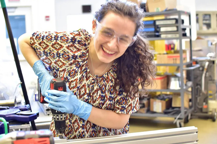 20250527-beneath-the-surface-why-bri-friedman-embraces-failure-lab A person wearing safety goggles and gloves uses a power tool in a lab.