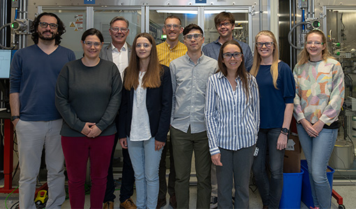 Continue reading about Ten people stand in front of laboratory equipment.